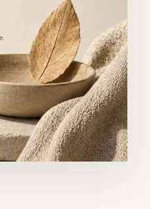 A gold-painted leaf resting in a handmade ceramic bowl beside woven linen.